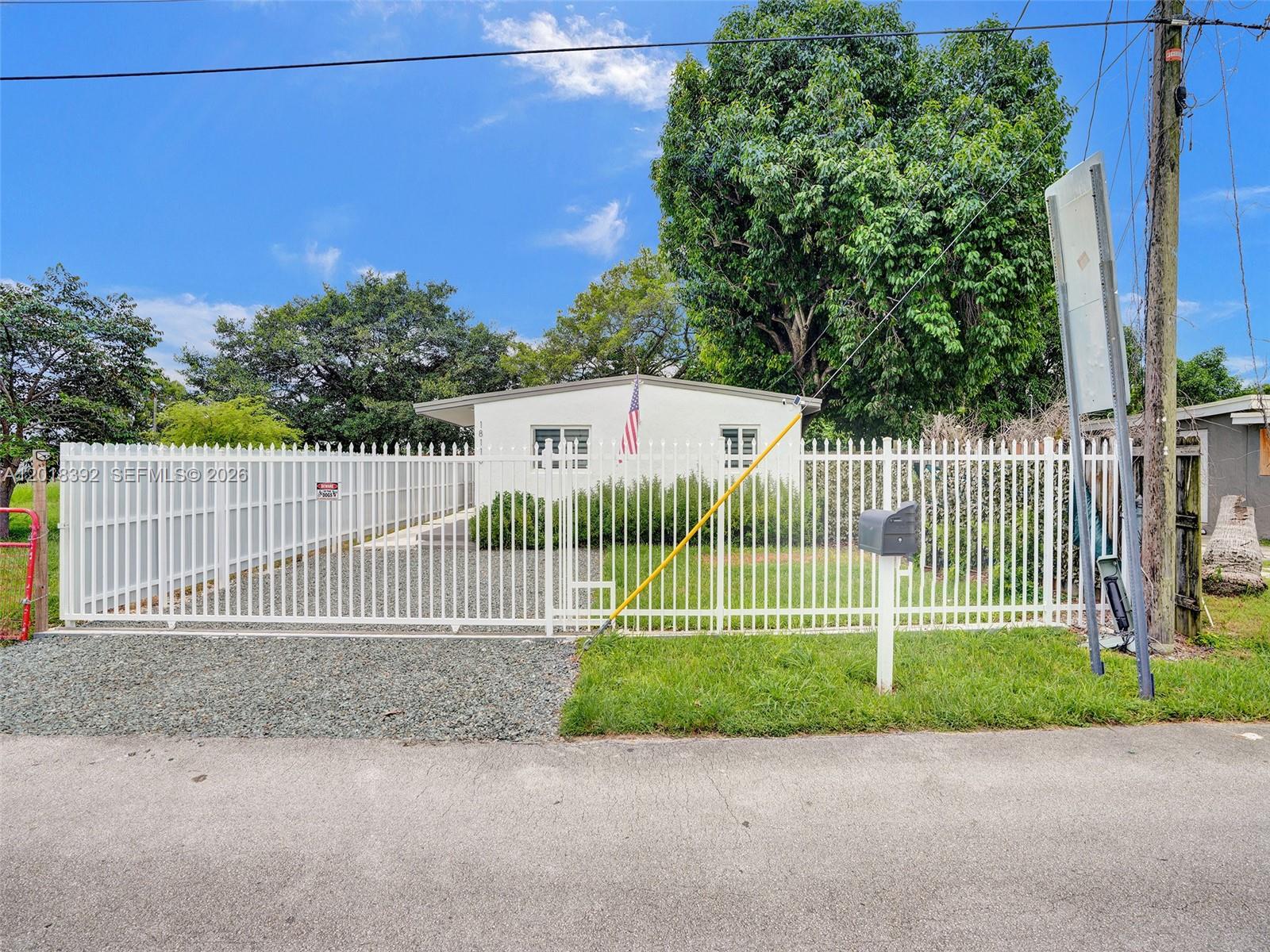 A white house with a fenced front yard and gravel driveway under a blue sky — 10222 SW 181st St, Miami FL 33157, MIAMI, FL
