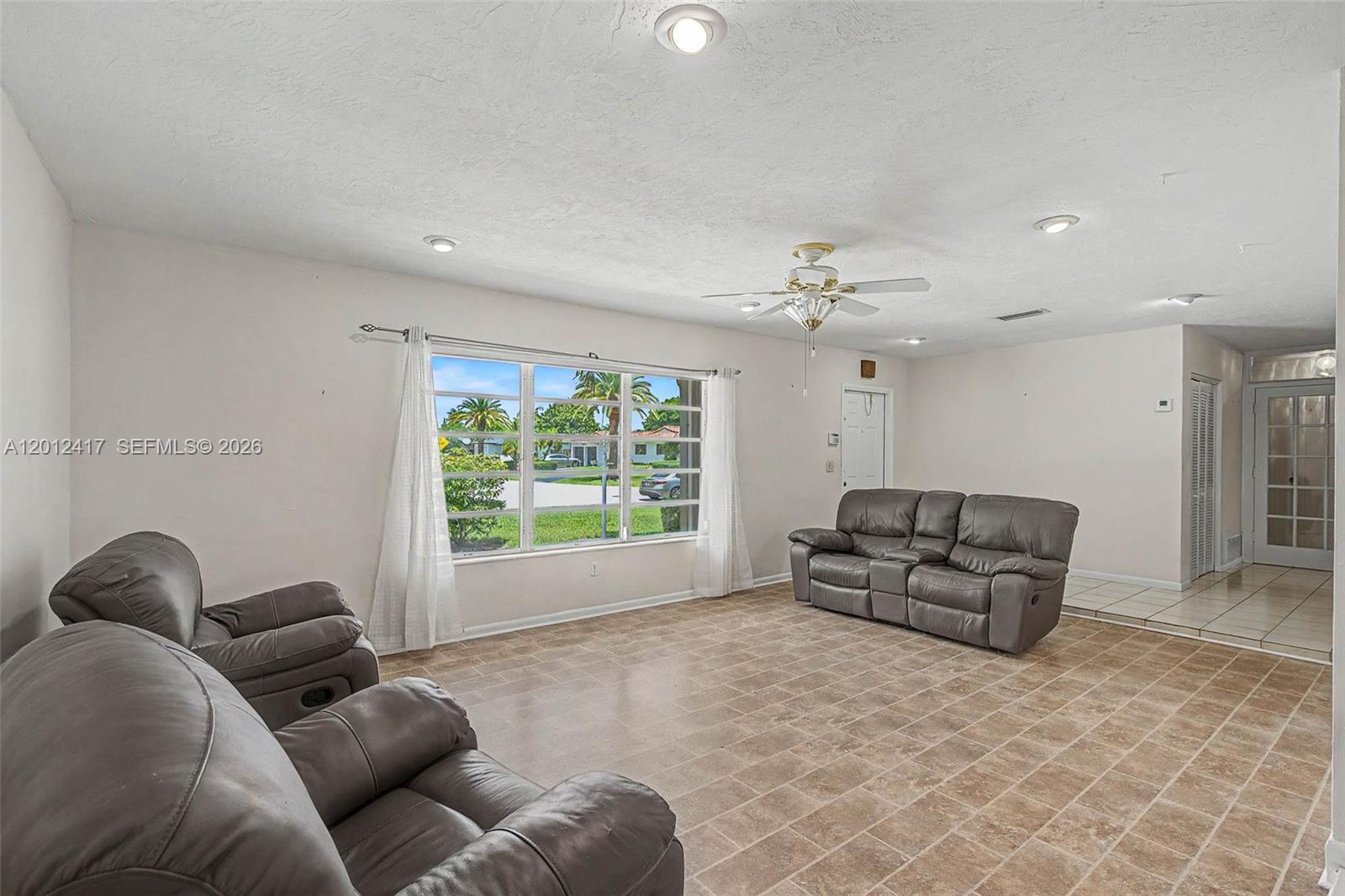 A living room features tile flooring, a ceiling fan, and a large window with curtains — 11380 SW 131st St, Miami FL 33176, MIAMI, FL