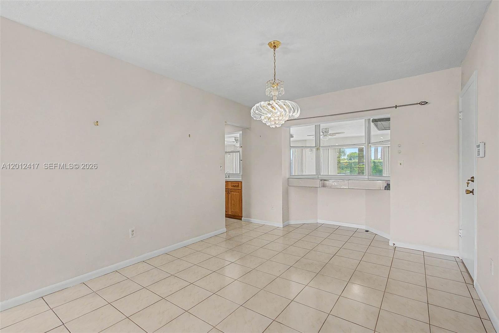 This dining room features light-colored tile flooring, a crystal chandelier, and a large window — 11380 SW 131st St, Miami FL 33176, MIAMI, FL