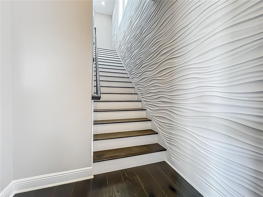A staircase with dark wood treads and white risers sits beside a textured wave-patterned wall — 13450 GABOR AVENUE, ORLANDO, FL