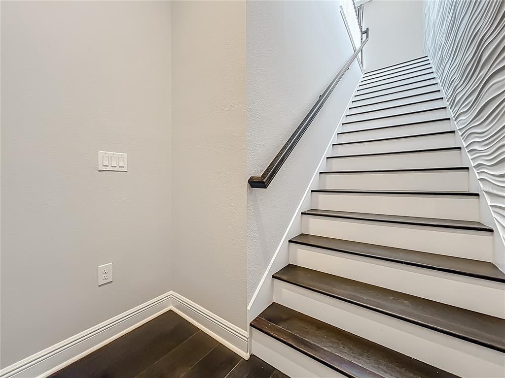A staircase with dark wood treads and white risers sits beside a textured accent wall — 13450 GABOR AVENUE, ORLANDO, FL