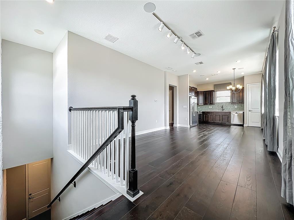 An open-concept living area with dark hardwood floors, a staircase railing, and a distant kitchen — 13450 GABOR AVENUE, ORLANDO, FL