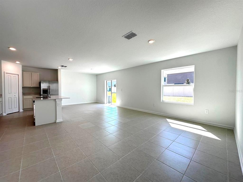 An open-concept living area features light tile flooring, a kitchen island, and a sliding glass door — 3874 AMERS LOOP, HAINES CITY, FL