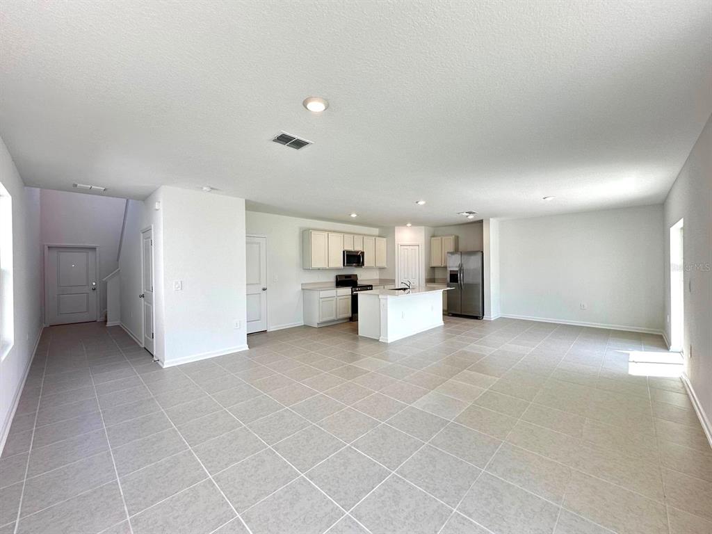 An open-concept kitchen and living area feature light-colored cabinets, a central island, and tile flooring — 3874 AMERS LOOP, HAINES CITY, FL