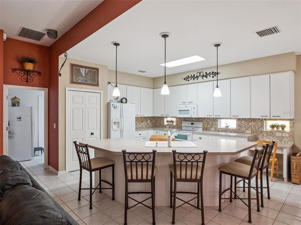 A kitchen features a large island with bar stools, white cabinetry, and tile flooring — 6100 PRINCE FREDERICK COURT, LEESBURG, FL