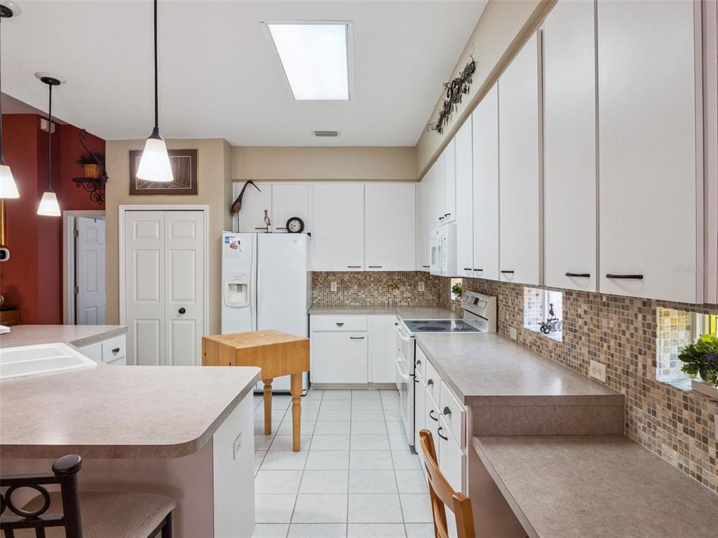A kitchen features white cabinets, a mosaic tile backsplash, laminate countertops, and a small island — 6100 PRINCE FREDERICK COURT, LEESBURG, FL