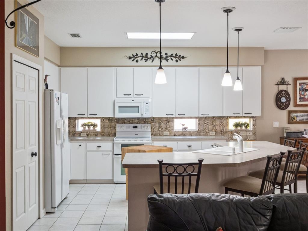 A kitchen features white cabinets, a central island with seating, and a tiled backsplash — 6100 PRINCE FREDERICK COURT, LEESBURG, FL