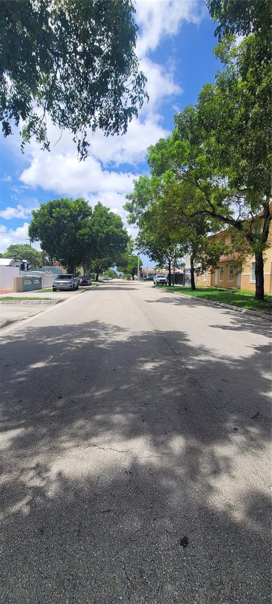 A paved street lined with mature trees and residential buildings under a blue sky — 33 E 20th St # 203, Hialeah FL 33010, HIALEAH, FL