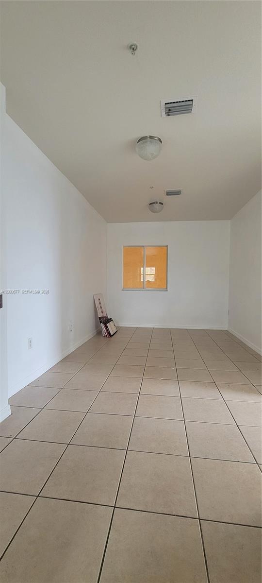 An empty room features white walls, tan tile flooring, and two ceiling-mounted light fixtures — 33 E 20th St # 203, Hialeah FL 33010, HIALEAH, FL