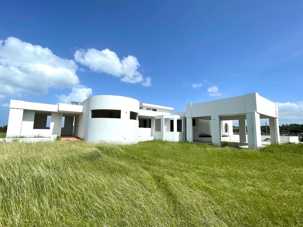 A modern, unfinished white concrete house stands in a field of tall grass — PR 311 KM 2.8 BO. GUANAJIBO SECTOR LAS DELICIAS, CABO ROJO, PR