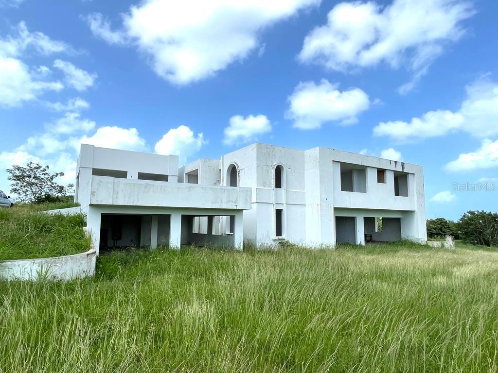 An unfinished white concrete house stands in a grassy field under a blue sky — PR 311 KM 2.8 BO. GUANAJIBO SECTOR LAS DELICIAS, CABO ROJO, PR