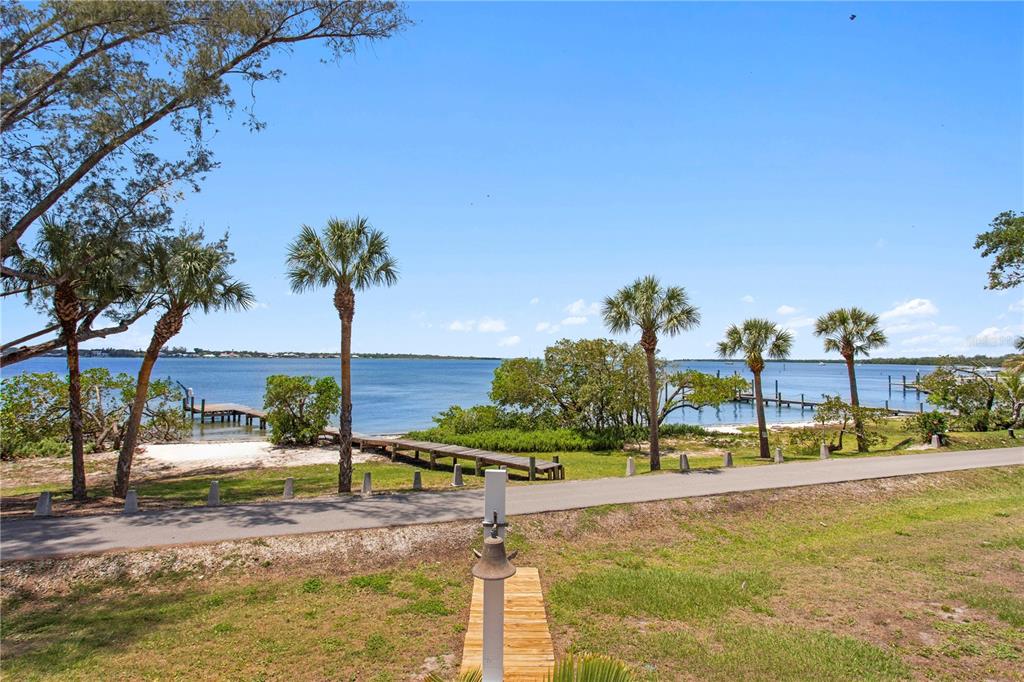 A view of a waterfront area with palm trees, a wooden dock, and a paved path — 5216 13TH STREET, PALMETTO, FL