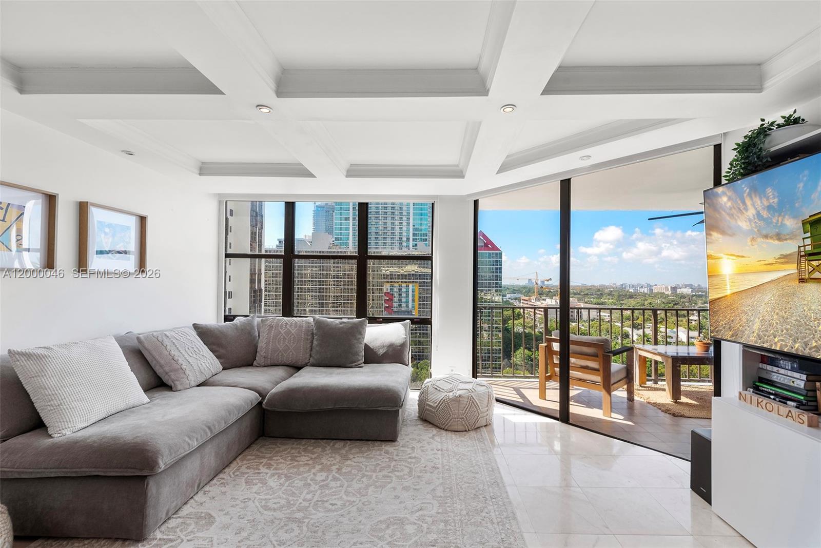 A modern living room features a grey sectional sofa, coffered ceiling, and a balcony view — 1915 Brickell Ave # C1612, Miami FL 33129, MIAMI, FL