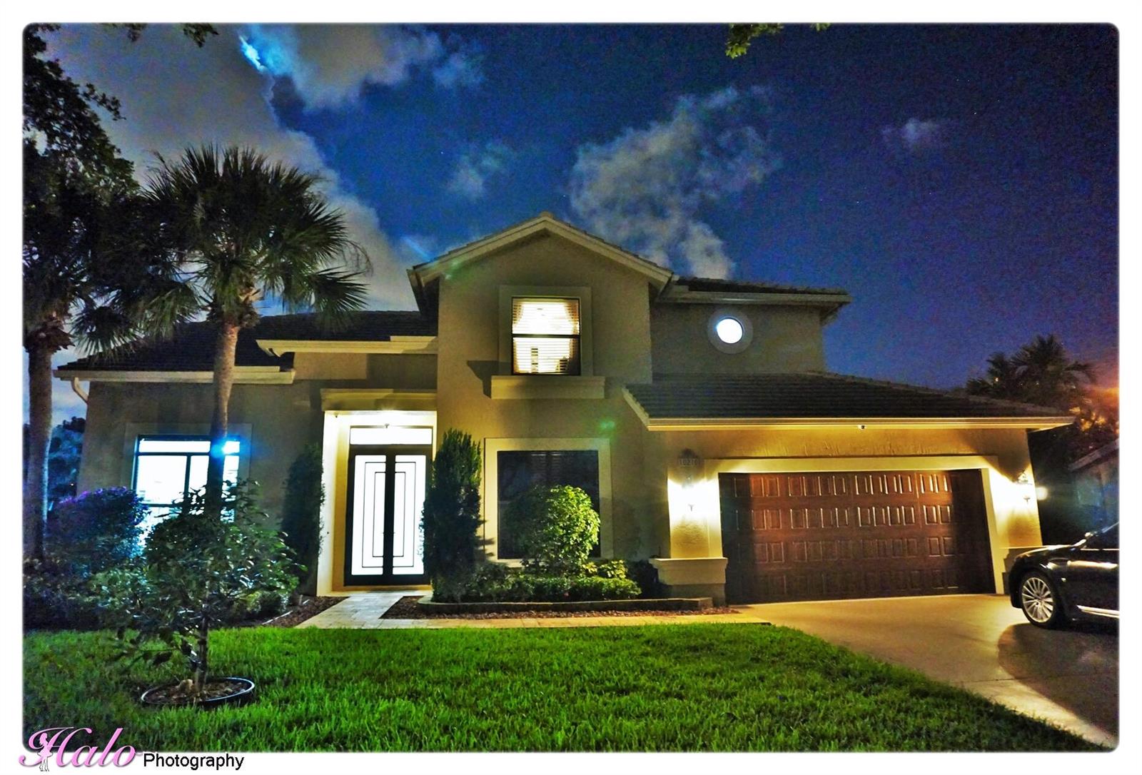 A two-story house exterior at night with a palm tree, garage, and illuminated windows — 10210 Lexington Estates Boulevard, Boca Raton FL 33428, BOCA RATON, FL