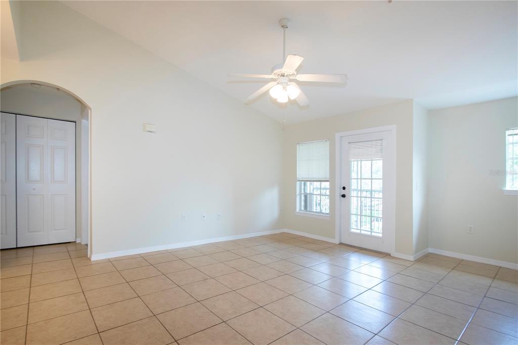 An empty room with beige tile flooring, a vaulted ceiling, a ceiling fan, and glass door — 7405 VISTA WAY UNIT 203, BRADENTON, FL