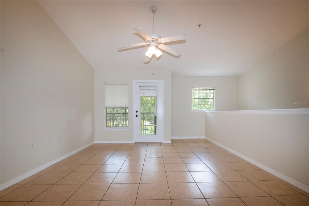 An empty room with beige tile flooring, a ceiling fan, and a glass-paneled exterior door — 7405 VISTA WAY UNIT 203, BRADENTON, FL