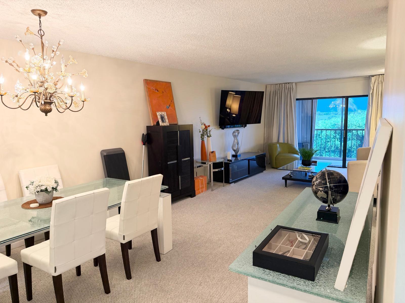 A combined dining and living area features a glass table, chandelier, and sliding glass doors — 3605 S Ocean Boulevard # A433, South Palm Beach FL 33480, SOUTH PALM BEACH, FL