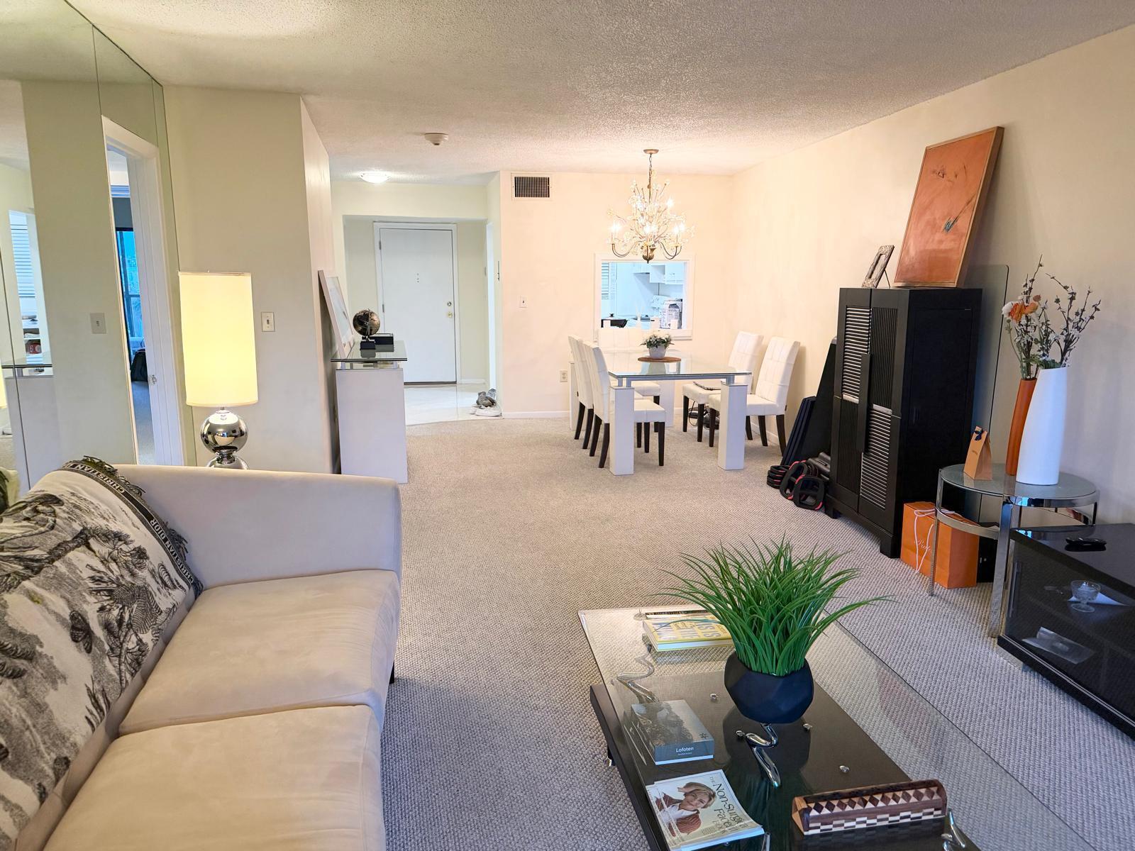 A living room and dining area with neutral carpeting, a glass coffee table, and chandelier — 3605 S Ocean Boulevard # A433, South Palm Beach FL 33480, SOUTH PALM BEACH, FL