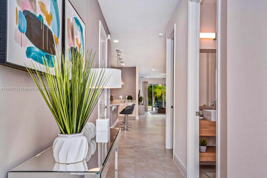 A hallway with tile flooring leads toward a kitchen and an outdoor patio area — 7700 Fairfax, Kissimmee FL 34747, KISSIMMEE, FL
