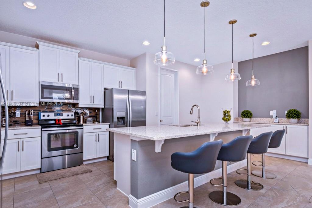 A modern kitchen features white cabinetry, stainless steel appliances, a granite island, and pendant lighting — 7700 Fairfax, Kissimmee FL 34747, KISSIMMEE, FL