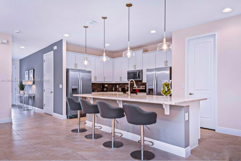 A kitchen features white cabinets, stainless steel appliances, a granite island, and three bar stools — 7700 Fairfax, Kissimmee FL 34747, KISSIMMEE, FL