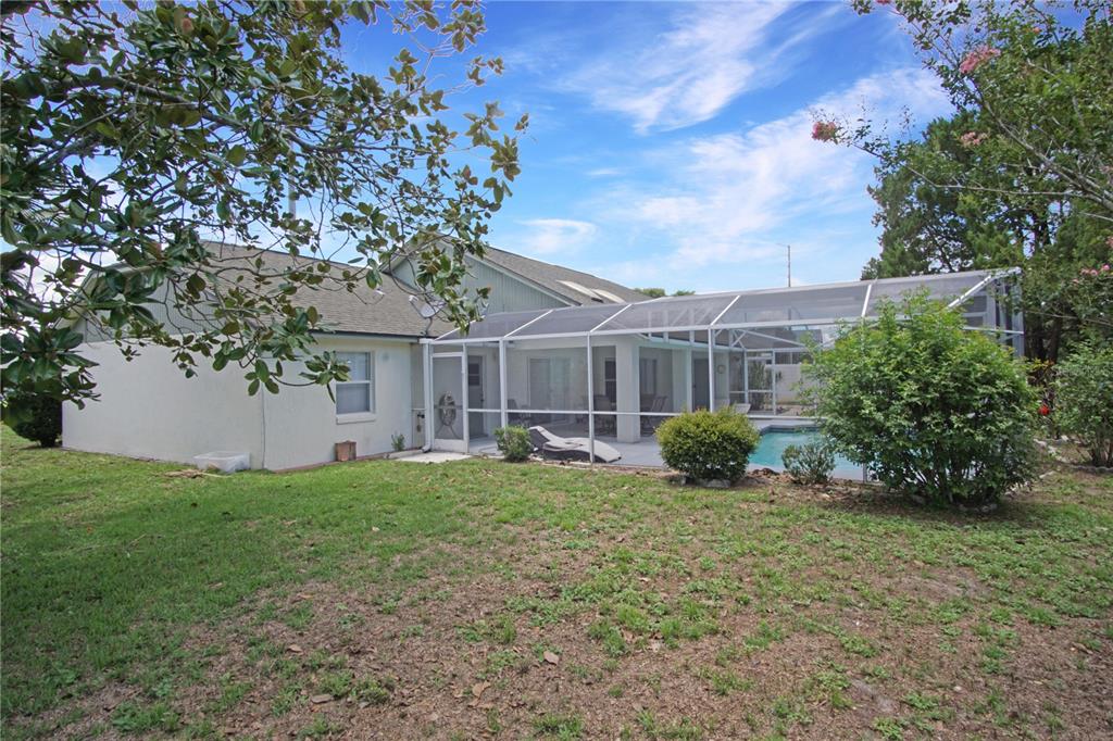 A backyard view of a house with a screened-in pool enclosure and a grassy lawn — 928 LOMA BONITA DRIVE, DAVENPORT, FL