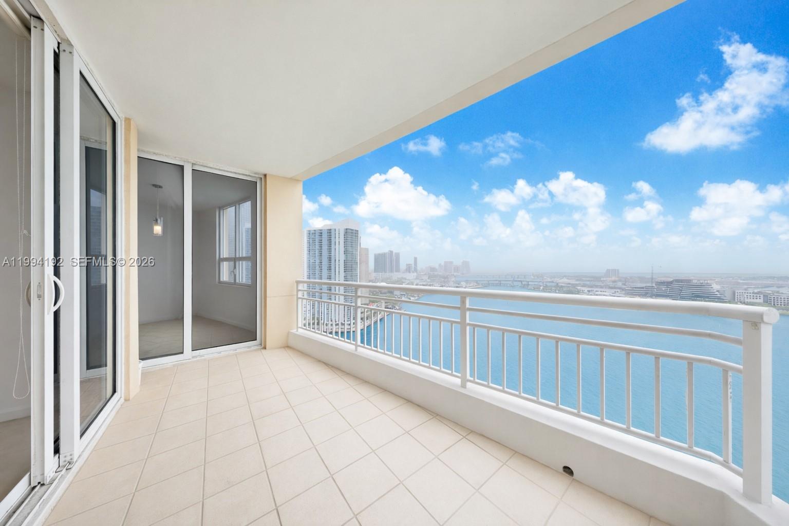 A balcony with white tile flooring and a metal railing overlooks a coastal city skyline — 848 Brickell Key Dr # 2702, Miami FL 33131, MIAMI, FL
