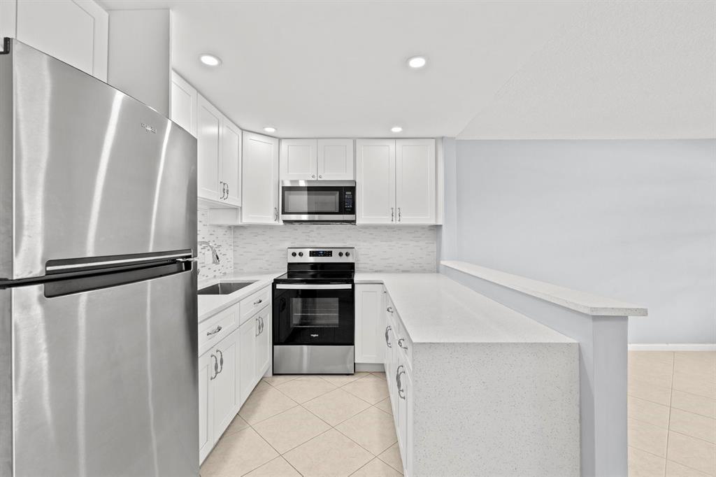 A modern kitchen features white cabinets, stainless steel appliances, and a quartz breakfast bar — 273 Prescott N, Deerfield Beach FL 33442, DEERFIELD BEACH, FL