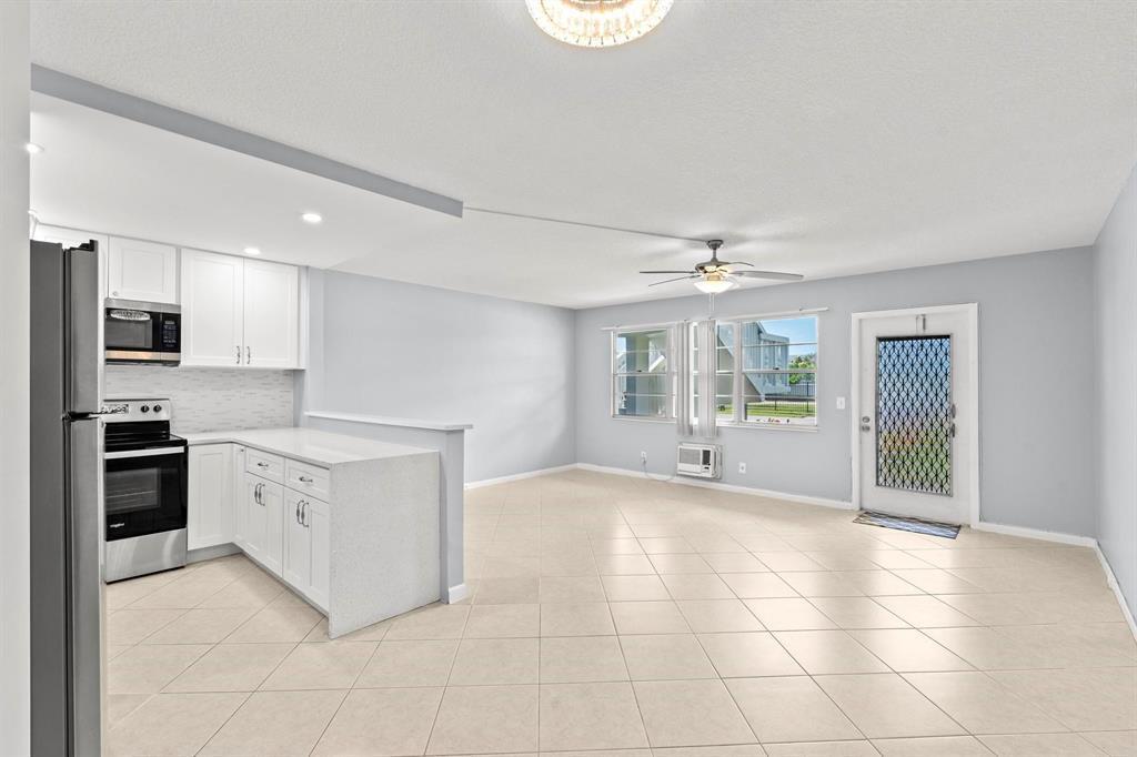 A kitchen with white cabinets and a living area with tile floors and a door — 273 Prescott N, Deerfield Beach FL 33442, DEERFIELD BEACH, FL