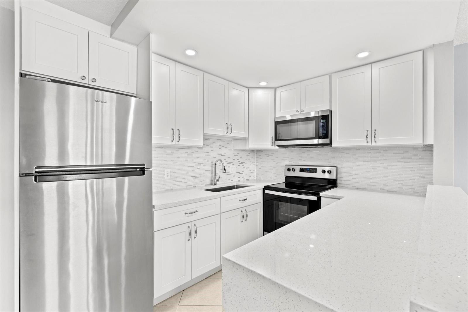 A modern kitchen features white cabinets, stainless steel appliances, and light-colored quartz countertops — 273 Prescott N, Deerfield Beach FL 33442, DEERFIELD BEACH, FL