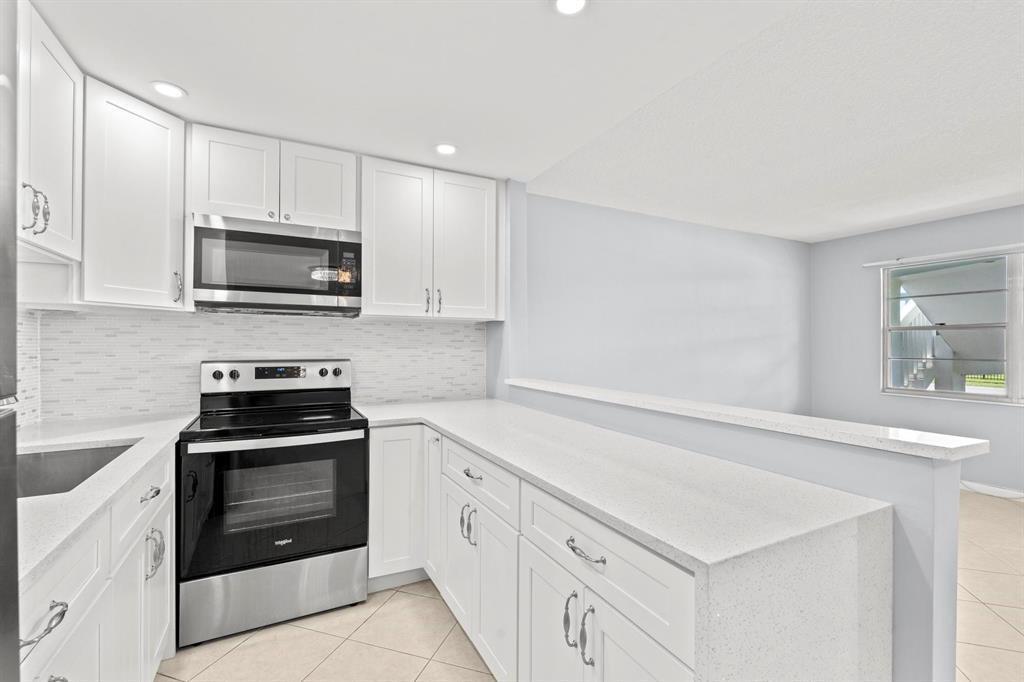 A kitchen with white cabinets, stainless steel appliances, and a quartz breakfast bar — 273 Prescott N, Deerfield Beach FL 33442, DEERFIELD BEACH, FL