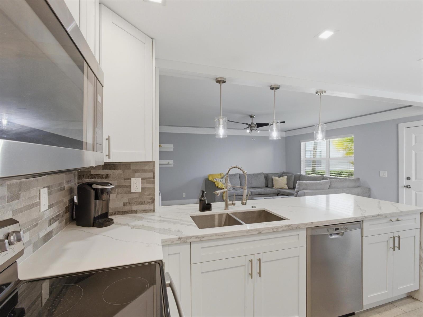 A kitchen with white cabinets, quartz countertops, and stainless steel appliances overlooks a living room — 397 Burgundy I, Delray Beach FL 33484, DELRAY BEACH, FL