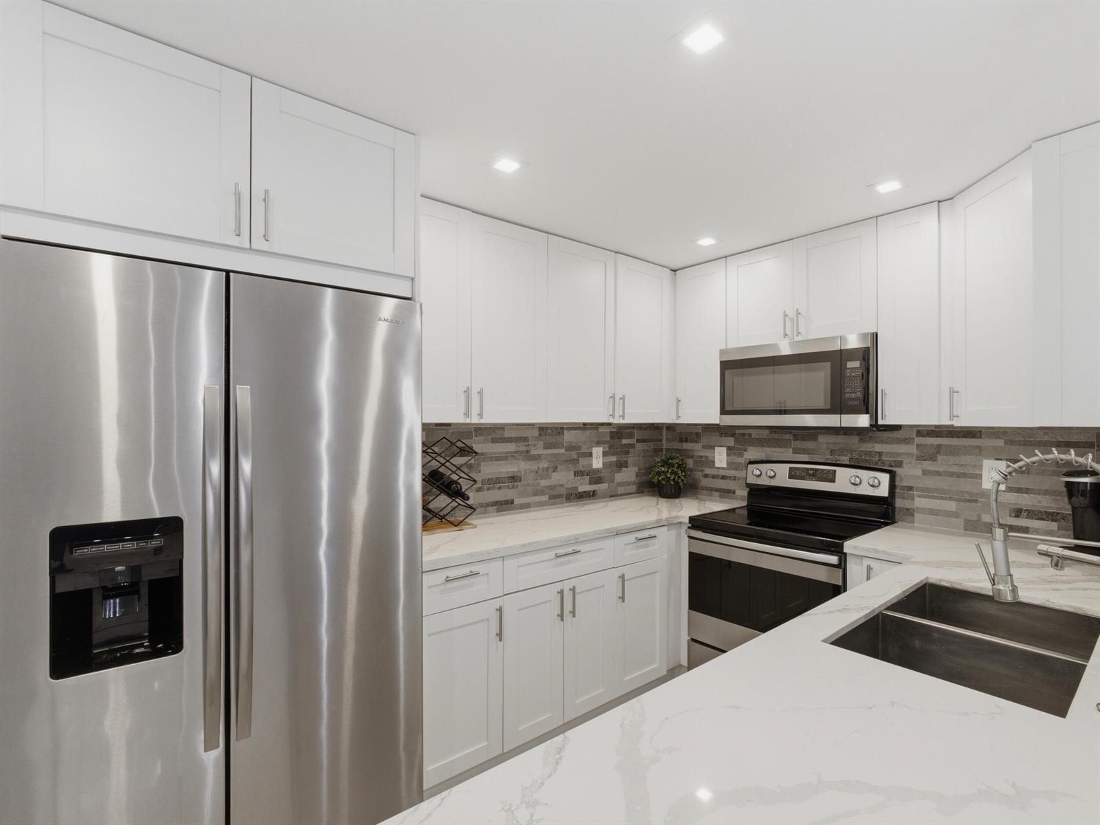 A modern kitchen features white cabinets, stainless steel appliances, and a marble-patterned countertop — 397 Burgundy I, Delray Beach FL 33484, DELRAY BEACH, FL