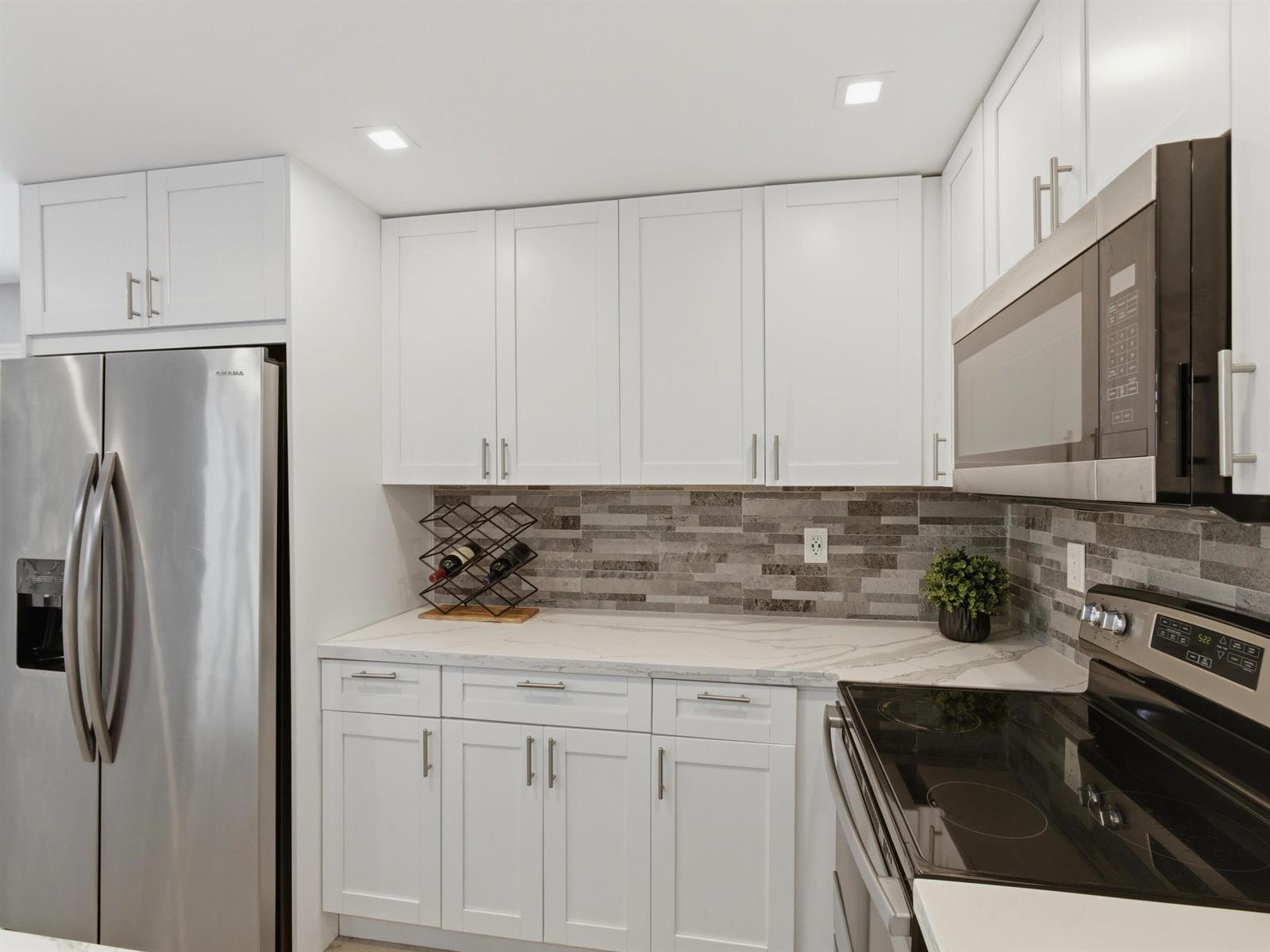 A kitchen features white cabinets, stainless steel appliances, a marble countertop, and a tiled backsplash — 397 Burgundy I, Delray Beach FL 33484, DELRAY BEACH, FL