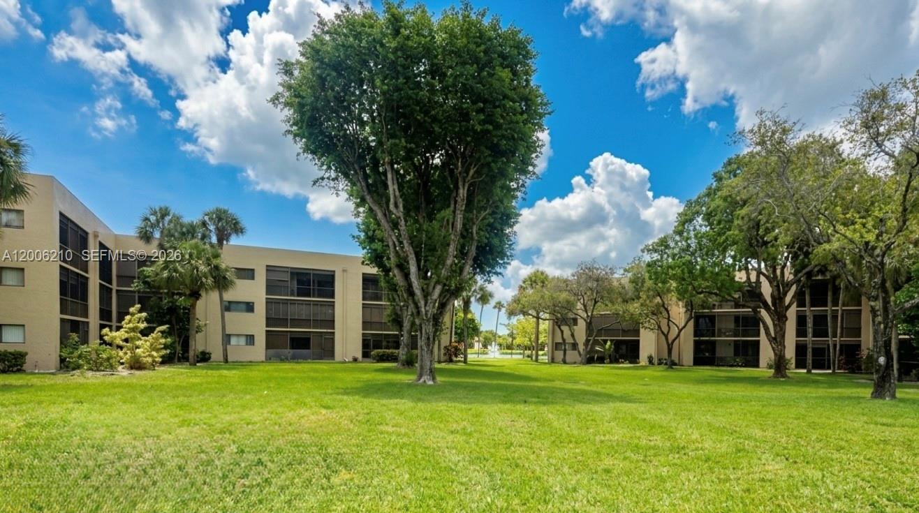 A grassy courtyard sits between two multi-story apartment buildings with screened balconies and trees — 5190 Las Verdes Cir # 115, Delray Beach FL 33484, DELRAY BEACH, FL