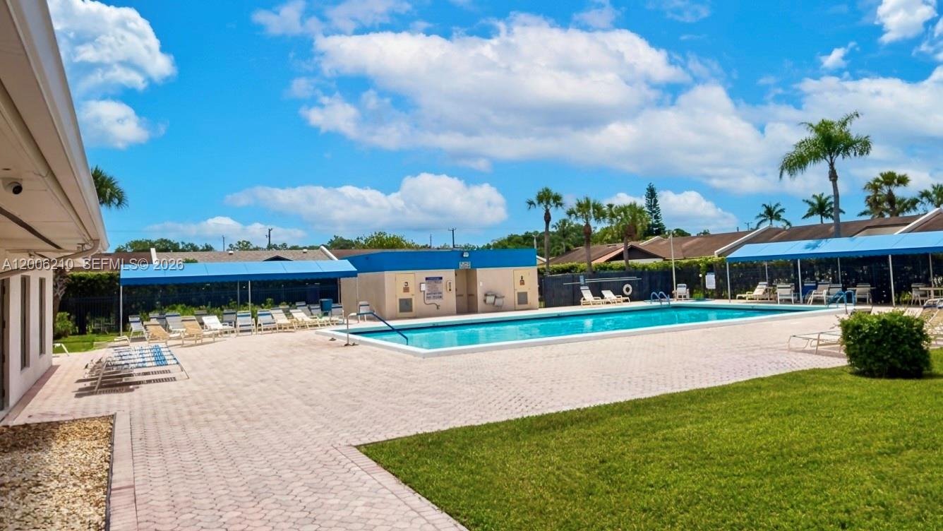 A rectangular swimming pool is surrounded by a paved deck, lounge chairs, and blue awnings — 5190 Las Verdes Cir # 115, Delray Beach FL 33484, DELRAY BEACH, FL