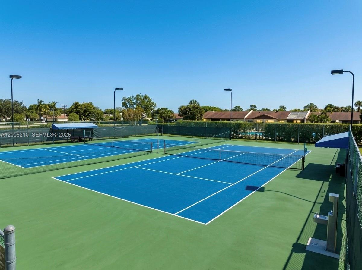 Two outdoor blue tennis courts are enclosed by a chain-link fence under a clear sky — 5190 Las Verdes Cir # 115, Delray Beach FL 33484, DELRAY BEACH, FL