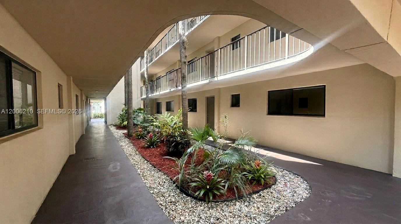 An outdoor walkway leads past a landscaped garden bed between two levels of apartment balconies — 5190 Las Verdes Cir # 115, Delray Beach FL 33484, DELRAY BEACH, FL