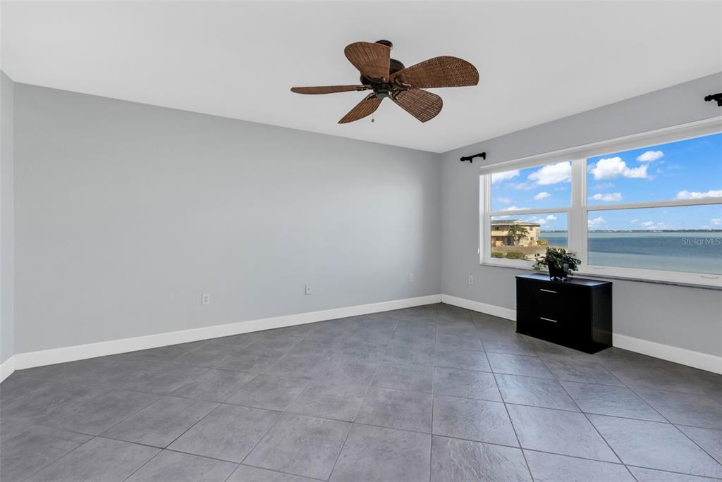 An empty room with gray walls, tile flooring, a ceiling fan, and a waterfront view — 1650 W MARION AVENUE UNIT 123, PUNTA GORDA, FL