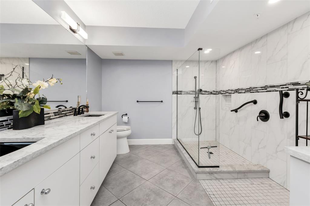 A modern bathroom features a white vanity, a walk-in glass shower, and gray tile flooring — 1650 W MARION AVENUE UNIT 123, PUNTA GORDA, FL