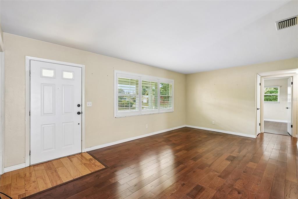 A living room with hardwood floors, a white front door, and a window with shutters — 1500 39TH STREET N, ST PETERSBURG, FL