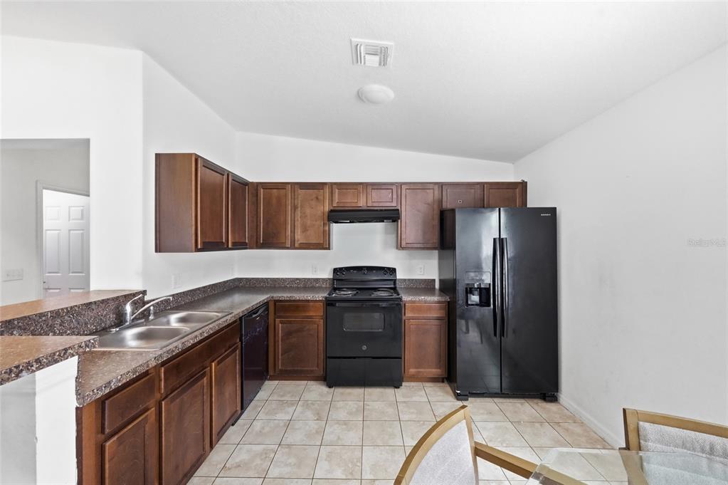 A kitchen with dark wood cabinets, black appliances, and a brown speckled countertop — 3640 GRUBBS STREET, MOUNT DORA, FL