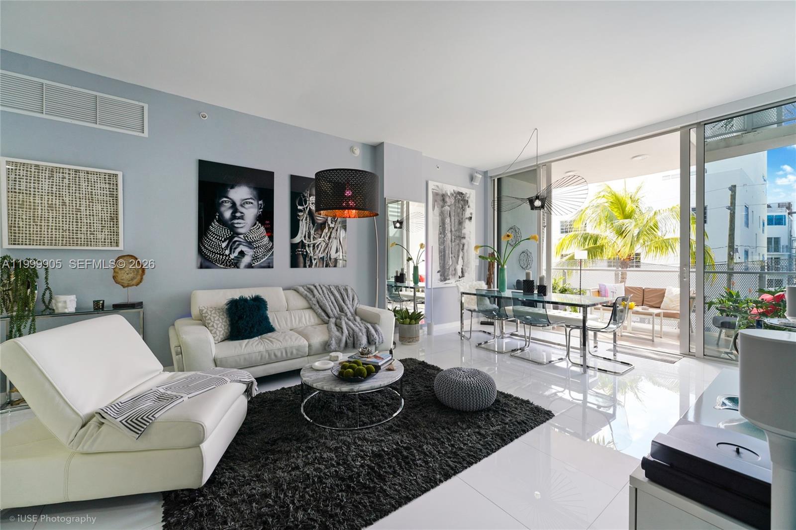 A modern living and dining area with white tile floors, a white sofa, and a balcony — 2100 Park Ave # 210, Miami Beach FL 33139, MIAMI BEACH, FL