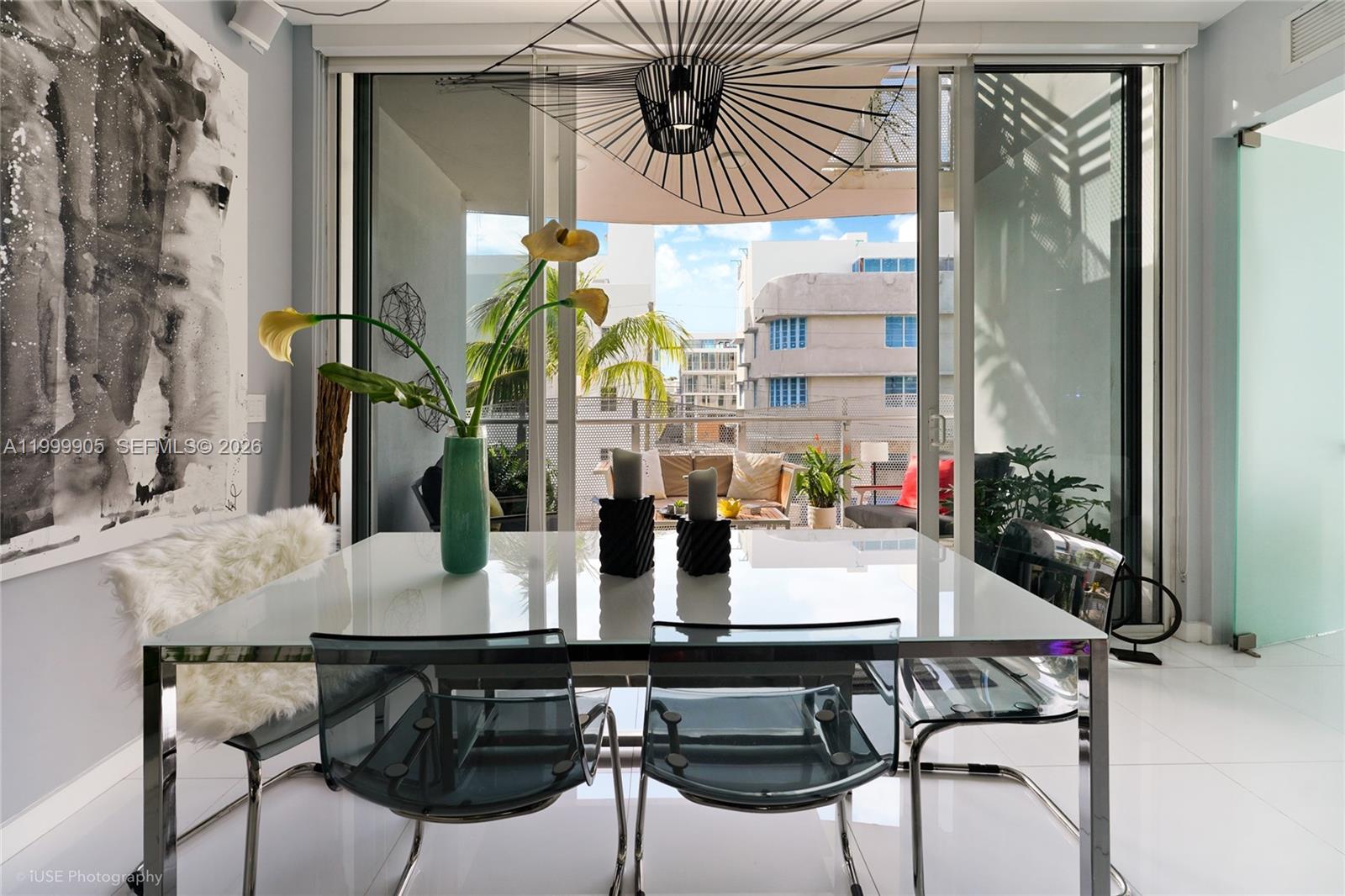 A dining room with a white table, transparent chairs, and a balcony view of buildings — 2100 Park Ave # 210, Miami Beach FL 33139, MIAMI BEACH, FL