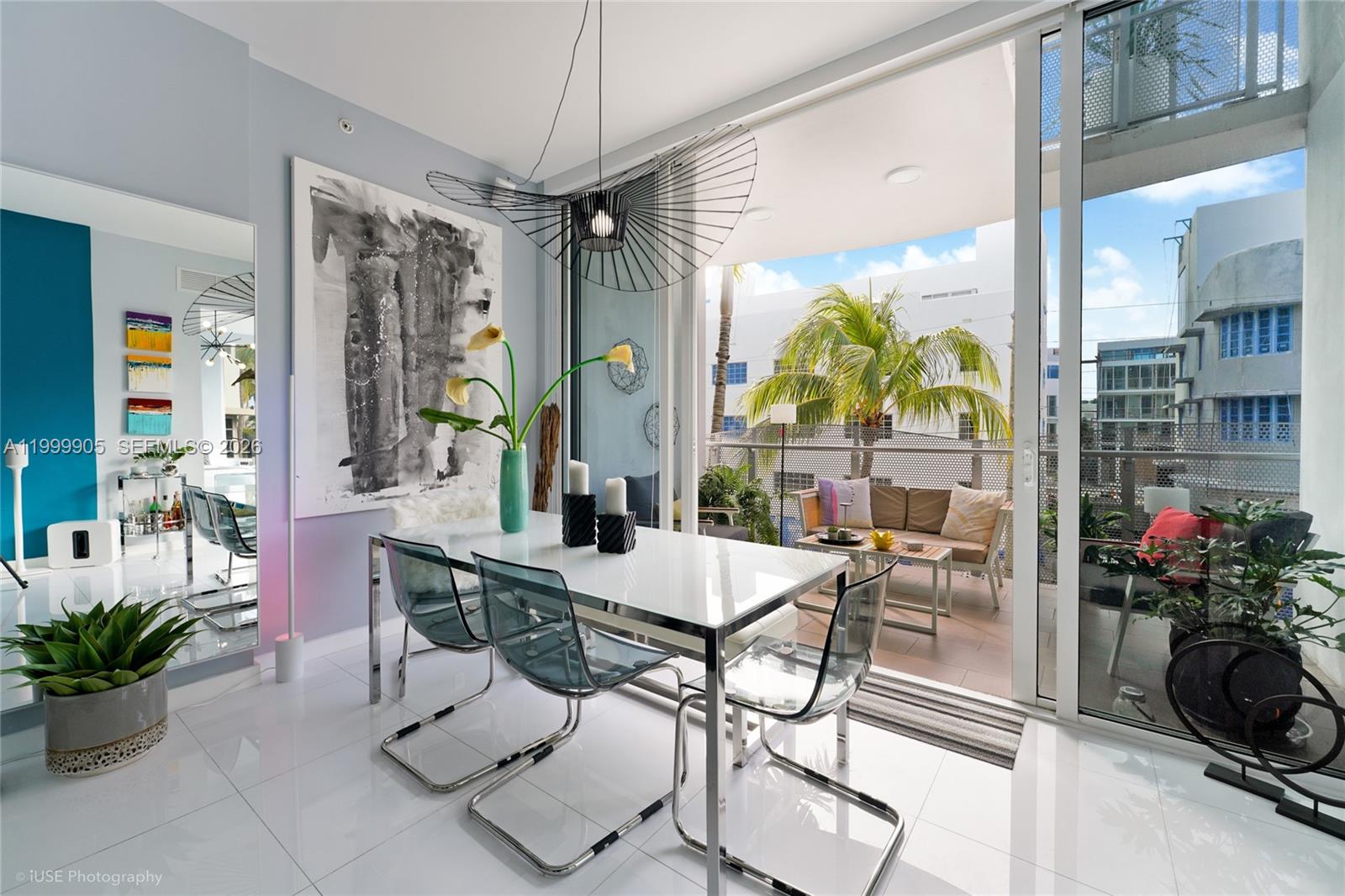 A modern dining room with a glass table, transparent chairs, and a balcony with outdoor seating — 2100 Park Ave # 210, Miami Beach FL 33139, MIAMI BEACH, FL