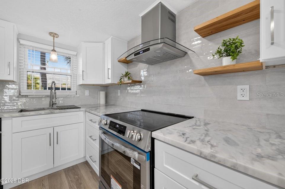A kitchen features white cabinets, marble-look countertops, a stainless steel range, and light wood shelving — 3131 S RIDGEWOOD AVENUE UNIT 108, SOUTH DAYTONA, FL