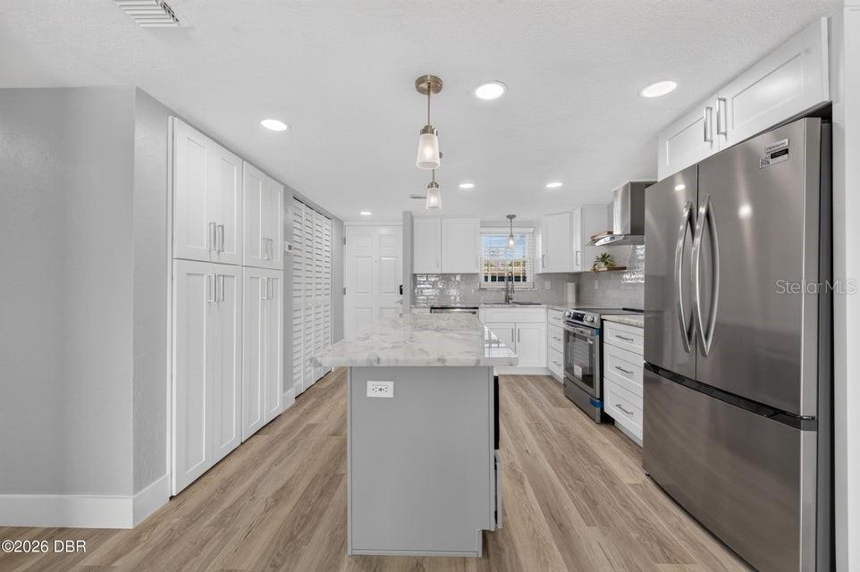 A kitchen features white cabinetry, a marble-topped island, stainless steel appliances, and wood-look flooring — 3131 S RIDGEWOOD AVENUE UNIT 108, SOUTH DAYTONA, FL