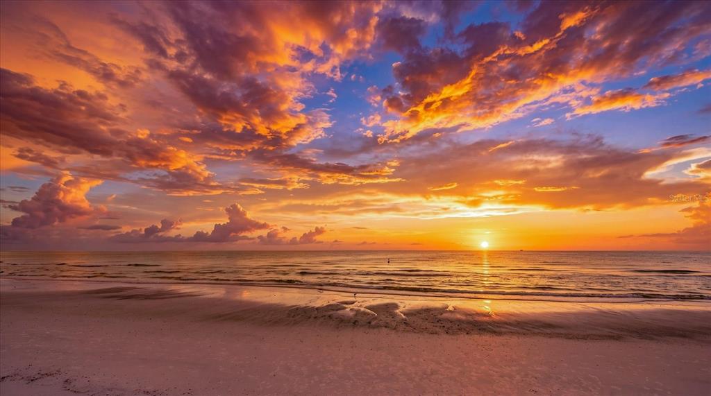 A vibrant sunset illuminates the sky over a sandy beach and the calm ocean water — 1621 GULF BOULEVARD UNIT 607, CLEARWATER BEACH, FL