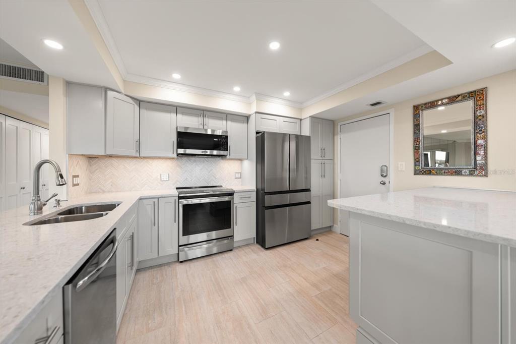 A modern kitchen features light gray cabinetry, stainless steel appliances, and white quartz countertops — 1621 GULF BOULEVARD UNIT 607, CLEARWATER BEACH, FL