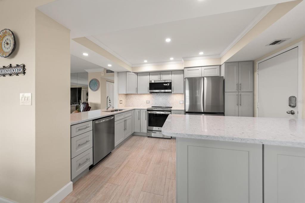 A kitchen features light gray cabinets, stainless steel appliances, and a white quartz countertop island — 1621 GULF BOULEVARD UNIT 607, CLEARWATER BEACH, FL